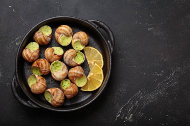 Sarımsak ve maydanozla pişirilmiş Bourgogne salyangozları, limon dilimleri ile servis edilen dökme demir tavada servis edilen lezzetli bir Fransız aperatifi, kopyalama alanı.