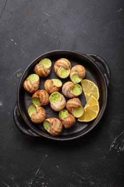 Sarımsak ve maydanoz tereyağıyla pişirilmiş Bourgogne salyangozları, limon dilimleri ile servis edilen dökme demir tavada servis edilen lezzetli bir Fransız aperatifi.