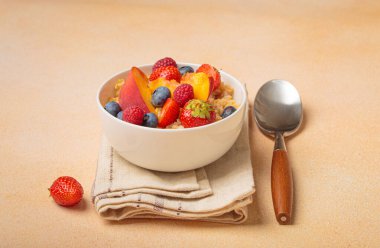 Taze yaban mersinli yulaf lapası, çilek, ahududu ve şeftali dilimleri sağlıklı ve besleyici bir kahvaltı için kaşıkla peçetede servis edilir.