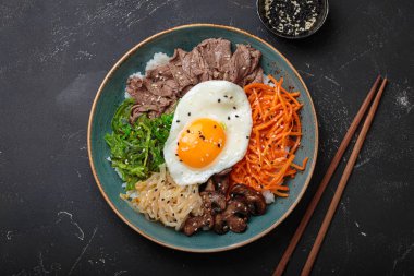 Bibimbap, haşlanmış pirinçli otantik Kore yemeği, kızarmış yumurta, sığır eti, renkli sebzeler, Kore 'nin geleneksel siyah arka plan manzarası.