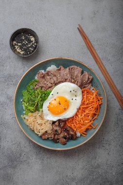 Bibimbap, haşlanmış pirinçli otantik Kore yemeği, kızarmış yumurta, sığır eti, renkli sebzeler, gri arka planda geleneksel Kore yemeği.