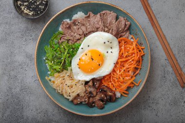 Bibimbap, haşlanmış pirinçli otantik Kore yemeği, kızarmış yumurta, sığır eti, renkli sebzeler, gri arka planda geleneksel Kore yemeği.
