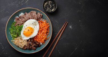 Bibimbap, haşlanmış pirinçli otantik Kore yemeği, kızarmış yumurta, sığır eti, renkli sebzeler, Kore 'nin geleneksel siyah arka plan manzarası.