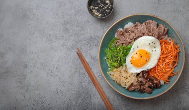 Bibimbap, haşlanmış pirinçli otantik Kore yemeği, kızarmış yumurta, sığır eti, renkli sebzeler, gri arka planda geleneksel Kore yemeği.