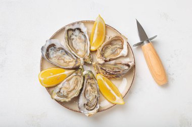 Limon dilimli bir tabağa yerleştirilmiş istiridye ve yanında istiridye bıçağı beyaz arka plan manzaralı bir deniz ürünleri sunumu.