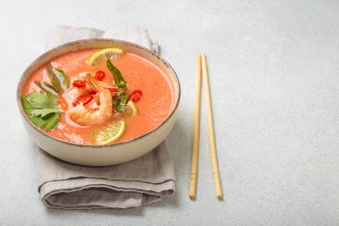 Taze karides, limon kamaları, şifalı otlar ve kırmızı biberlerle süslenmiş ve yanında keten peçetede yemek çubukları bulunan Tayland 'ın popüler bir yemeği olan kremalı Tom yum çorbası bir kâse içinde servis edilir.