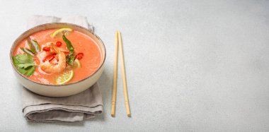 Taze karides, limon kamaları, şifalı otlar ve kırmızı biberlerle süslenmiş ve yanında keten peçetede yemek çubukları bulunan Tayland 'ın popüler bir yemeği olan kremalı Tom yum çorbası bir kâse içinde servis edilir.