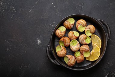 Sarımsak ve maydanozla pişirilmiş Bourgogne salyangozları, limon dilimleri ile servis edilen dökme demir tavada servis edilen lezzetli bir Fransız aperatifi, kopyalama alanı.