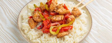 Lezzetli tavuk kızartması rengarenk dolma biberleri ve pofuduk pirinçle birlikte, yemek çubuklarıyla servis edilmiş, Asya 'dan esinlenilmiş lezzetli yemekler.