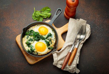 Tahta bir tahtanın üzerinde ıspanaklı iki sahanda yumurta, sağlıklı bir kahvaltı.