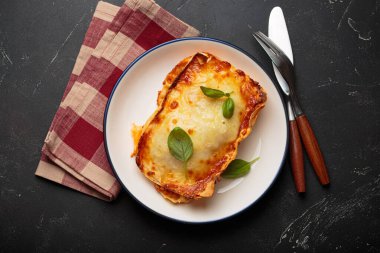 Lazanya, geleneksel İtalyan yemeği, zengin domates sosu ve erimiş peynirle pişirilmiş, taze fesleğen yapraklarıyla süslenmiş, koyu arkaplanda lezzetli bir yemek.