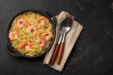 Siyah dökme demir tavada servis edilen karidesli makarna taze limon dilimleri ve siyah kırsal arka planda maydanoz üst görünümü ile süslenmiş, kopyalama alanı