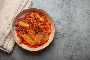 Kimchi, mayalanmış bir Napa lahanası Kore yemeği, gri beton bir arka planda seramik bir kasede keten peçeteyle, canlı rengini ve dokusunu yukarıdan aşağıya doğru yakalıyor, boşluğu kopyalıyor.