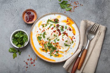 Türk yumurtaları cilbir, lezzetli ve renkli bir kahvaltı yoğurt üzerinde haşlanmış yumurta, baharatlar ve taze otlarla tatlandırılmış, gri beton arka planda düzenlenmiş