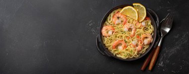 Siyah dökme demir tavada servis edilen karidesli makarna taze limon dilimleri ve siyah kırsal arka planda maydanoz üst görünümü ile süslenmiş, kopyalama alanı