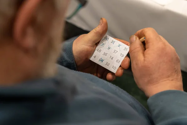 stock image Over the shoulder view of old man holding bingo card with numbers crossed out and pencil