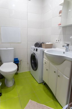 Banyonun içinde beyaz lavabo, tuvalet ve çamaşır makinesi var.