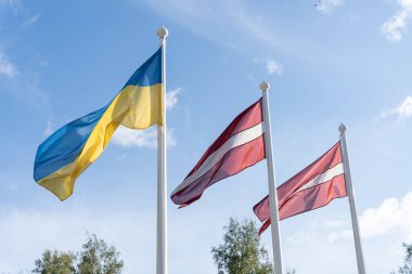 Ukrayna ve Letonya bayrakları rüzgarda dalgalanan bayrak direkleri üzerinde birlikte