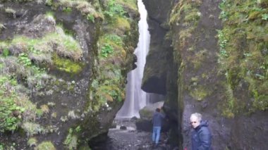 Seljalandsfoss, İzlanda - 06.22.2023: İzlanda 'daki kayalıkların arkasında Gljufrafoss veya Gljufrabui şelalesinin fotoğraflarını çeken turistler