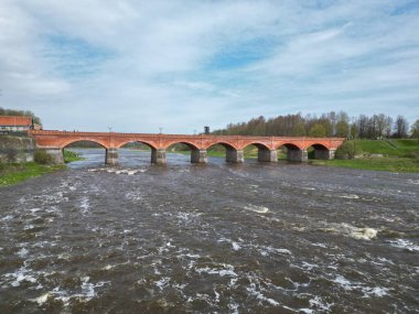 The old red brick bridge across the Venta river. Kuldiga, Latvia clipart