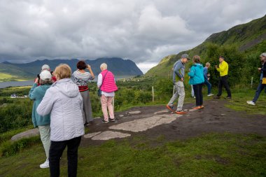 Norveç - 07.07.2024: Norveç 'te yeşil dağlara bakan turistler, fiyort ve mavi gökyüzü