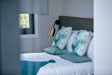 Modern yatak odası, beyaz yatak odası, dekoratif yastıklar, ve duvarla döşenmiş şık bir lamba..