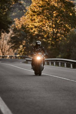 Güz ağaçları tarafından çerçevelenmiş bir yolda kameraya doğru giden bisikletli.