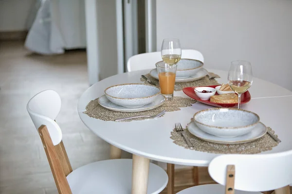 Modern dining table set with plates, glasses, and bread in a bright room.