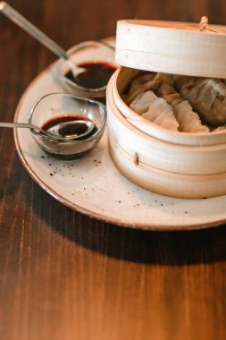 Daha büyük bir ahşap kasenin yanında iki küçük sos kabı bulunan taze gyozas içeren bir tabağın ayrıntılı görüntüsü..