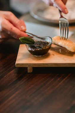 Bıçak ve çatal tutan bir adamın elleri, tahta bir masadan bir parça ekmek topluyor..