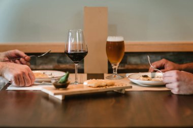 İki erkek eli, bir şarap kadehi, bir bira, bir restoran menüsü ve her biri yemek için hazır kap kacak taşıyan ahşap bir tabak.