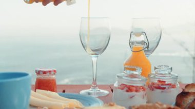 Outdoor Breakfast Setting with Fresh Orange Juice Being Poured into a Glass, Accompanied by Assorted Breakfast Items Overlooking a Serene Ocean View