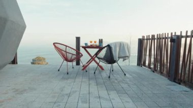 Scenic Outdoor Breakfast Setup with Modern Chairs and a Table Overlooking the Ocean, Featuring Fresh Orange Juice and Various Breakfast Items