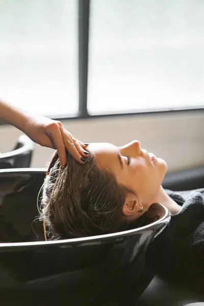 Bir kadın, kuaför salonunda kafa masajından zevk alır. Sahne, yumuşak doğal ışıklandırmayla modern bir salon dekorunu yakalıyor..