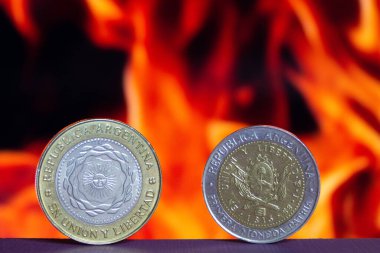 Rio Gallegos, Arjantin - 20 Mayıs 2023: Bir peso sikke ve iki Arjantin peso sikkesi bir yüzeyde duruyor ve odağını kaybetmiş bir yangın, enflasyon veya ekonomik kriz kavramı