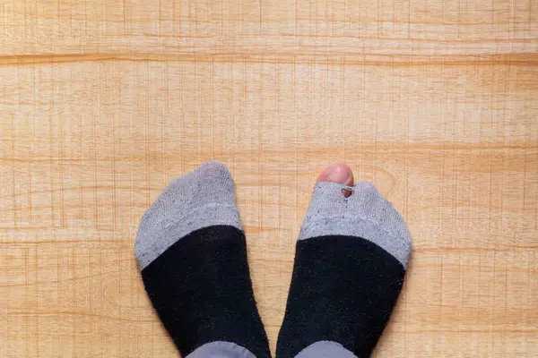 stock image feet wearing torn stockings with the big toe sticking out of a hole,on a wooden background,concept of need or comfort at home