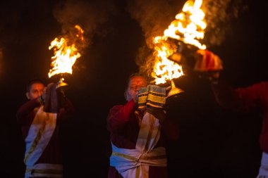 Rishikesh, Uttarakhand, India - October 2022: Portrait of hindu male priests performing river Gange aarti with fire flame in hands at triveni ghat to worship river ganges. Ganga aarti performed in night.