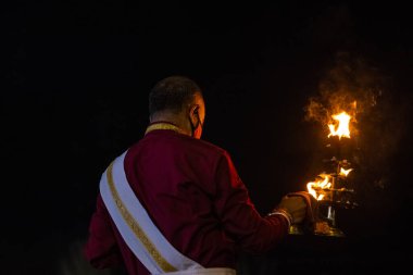 Rishikesh, Uttarakhand, India - October 2022: Portrait of hindu male priest performing river Gange aarti with fire flame in hand at triveni ghat to worship river ganges. Ganga aarti performed in night