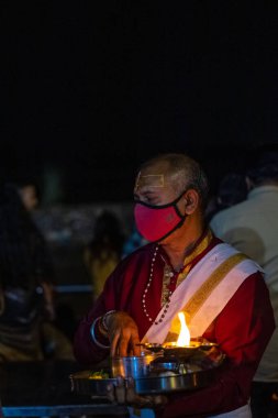 Rishikesh, Uttarakhand, India - October 2022: Portrait of hindu male priest performing river Gange aarti with fire flame in hand at triveni ghat to worship river ganges. Ganga aarti performed in night