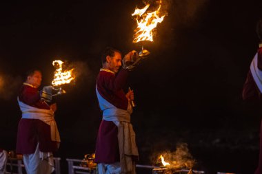 Rishikesh, Uttarakhand, India - October 2022: Portrait of hindu male priests performing river Gange aarti with fire flame in hands at triveni ghat to worship river ganges. Ganga aarti performed in night.
