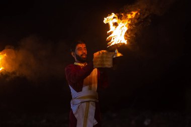 Rishikesh, Uttarakhand, India - October 2022: Portrait of hindu male priest performing river Gange aarti with fire flame in hand at triveni ghat to worship river ganges. Ganga aarti performed in night