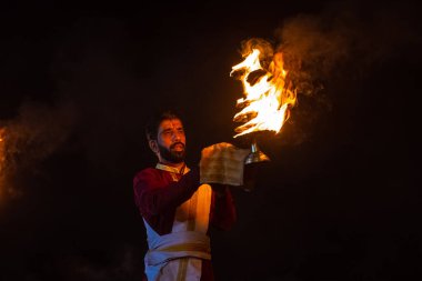 Rishikesh, Uttarakhand, India - October 2022: Portrait of hindu male priest performing river Gange aarti with fire flame in hand at triveni ghat to worship river ganges. Ganga aarti performed in night