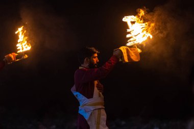 Rishikesh, Uttarakhand, India - October 2022: Portrait of hindu male priest performing river Gange aarti with fire flame in hand at triveni ghat to worship river ganges. Ganga aarti performed in night