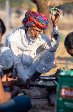 Pushkar, Rajasthan, India - November 2022: Pushkar Fair, Portrait of an camel trader in ethnic dress and rajasthani turban on smoking fair ground during pushkar fair.