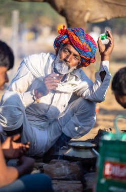 Pushkar, Rajasthan, India - November 2022: Pushkar Fair, Portrait of an camel trader in ethnic dress and rajasthani turban on smoking fair ground during pushkar fair.