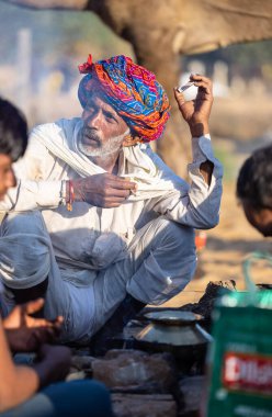 Pushkar, Rajasthan, India - November 2022: Pushkar Fair, Portrait of an camel trader in ethnic dress and rajasthani turban on smoking fair ground during pushkar fair.