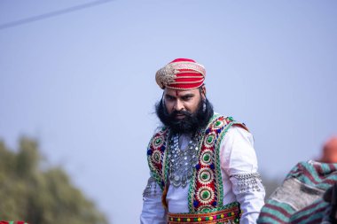Bikaner, Rajasthan, India - January 2023: Camel Festival, Portrait of an young male with beard in traditional dress sitting on camel cart while participating in parade. Selective focus.