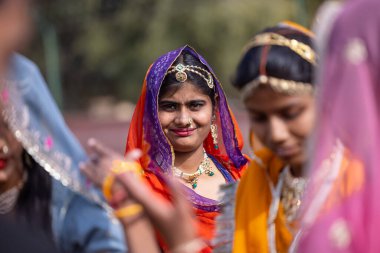Bikaner, Rajasthan, Hindistan - Ocak 2023: Deve Festivali Bikaner, geçit törenine katılırken geleneksel Rajasthan elbiseleri ve mücevherleriyle genç güzel kızlardan oluşan bir grup. Seçici odak.