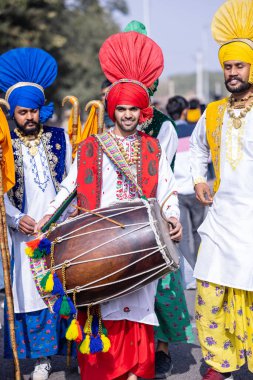 Bikaner, Rajasthan, India - January 2023: Punjabi Bhangra, Portrait of young sikh male in traditional punjabi colorful dress and turban performing bhangra dance with smile in camel festival with focus