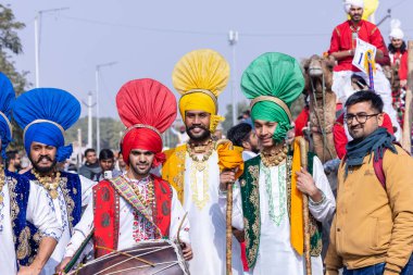 Bikaner, Rajasthan, India - January 2023: Punjabi Bhangra, Portrait of young sikh male in traditional punjabi colorful dress and turban performing bhangra dance with smile in camel festival with focus